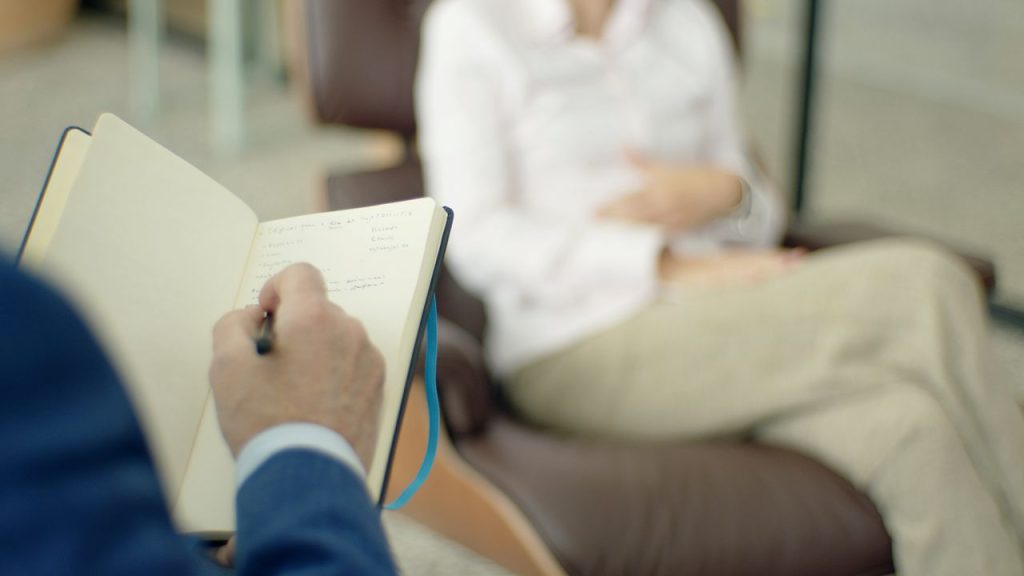 Therapist writing notes during a counseling session with a client.